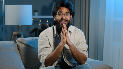 Arabic happy motivated man watching TV at home at night late in evening. Spaniard bearded Indian...