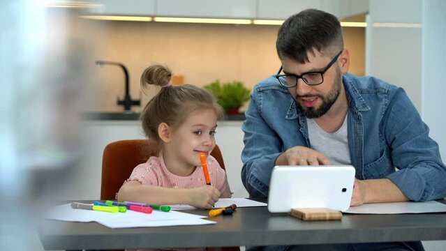 Father and little girl watch video tutorial on tablet and learn to draw on internet at home. Drawing training. Online education concept.