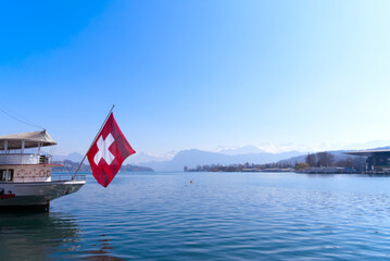 Stern of passenger ship at Lake Lucerne with waving Swiss flag ans Swiss Alps in the background on a sunny spring day. Photo taken March 23rd, 2022, Lucerne, Switzerland.