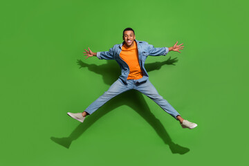 Fototapeta na wymiar Full body photo of overjoyed sportive man jumping up have fun wear denim clothes isolated on green color background