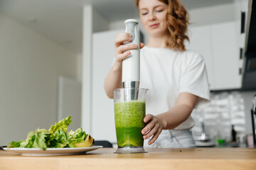Woman preparing green smoothie in her kitchen