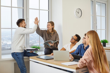 Overjoyed multiethnic millennial students give high five work together on computer. Smiling diverse...