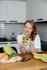 Young slim caucasian woman drinking green smoothie in the kitchen