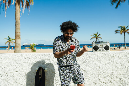 African Man Having Fun Doing Selfie With Mobile Phone With Beach On Background - Focus On Face