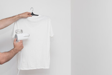 Steam the T-shirt with a portable steamer on a white background. copyspace - obrazy, fototapety, plakaty