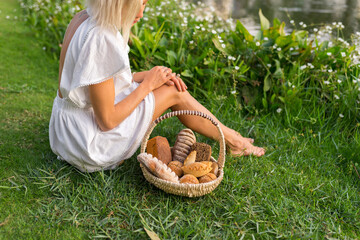 Young woman in white dress sitting on the grass with basket with assorti of brown and white homemade bread. High quality photo