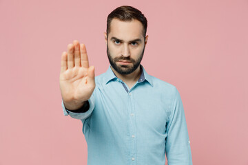 Young sad angry strict man 20s wearing classic blue shirt showing stop gesture with palm refusing...