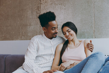 Two young friends smiling happy fun woman man of African American ethnicity 20s in casual clothes hugging sitting on gray sofa indoor spend free time rest in flat together. People lifestyle concept. - obrazy, fototapety, plakaty