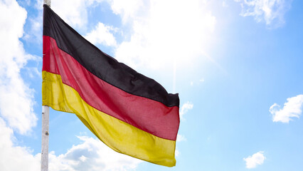 The official flag of Germany waving on a blue sky background. Horizontal banner design, with the German flag hanging on a sunny background with white clouds. Deutschland flag wide banner