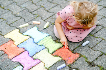 Little preschool girl painting with colorful chalks on ground on backyard. Positive happy toddler...