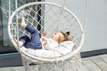 Cute little caucasian baby girl is relaxing and having fun in hammock swing in backyard.
