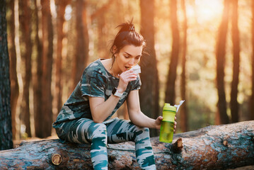 Fit woman eating energy granola bar after running at sunset in the forest