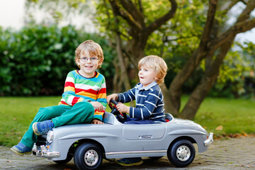 Two little preschool boys playing with big old toy car in summer garden, outdoors. Happy children play together, driving car. Outdoor activity for kids. Siblings and friends on warm day