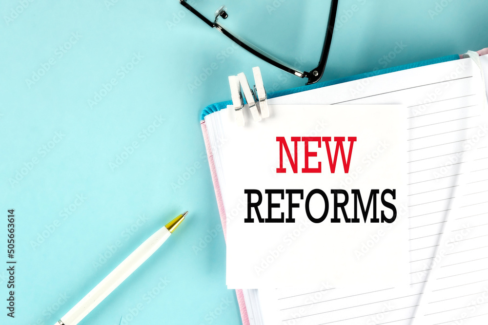 Poster new reforms text on a sticky on notebook with pen and glasses , blue background