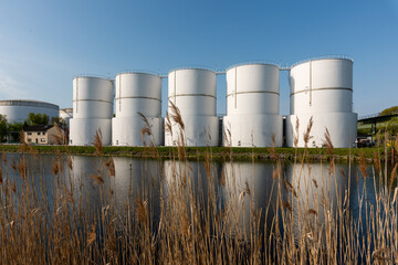Oil supply. large white steel reservoirs of a tank farm for mineral oil at a canal.