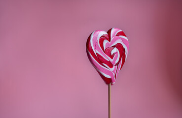 Vertical photo of  festive sweets for  beloved  Pink  background. Sweet heart shaped candy on stick. Romantic valentine day food. Heart shaped lollipop close up.