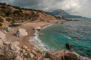 The sandy shore of the Black Sea with stone boulders. Surf with turquoise water