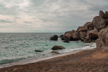 Sandy seashore with stone boulders. Surf with turquoise water.