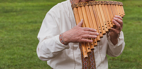 Musician man in vyshyvanka plying sopilka rebro ethnic woodwind musical instrument. Pan flute, panpipes syrinx, multiple pipes of gradually increasing length. Ukraininan folk music festival in Ukraine