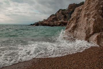 Sandy seashore with stone boulders. Surf with turquoise water.