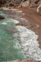 Sandy seashore with stone boulders. Surf with turquoise water. Vertical image
