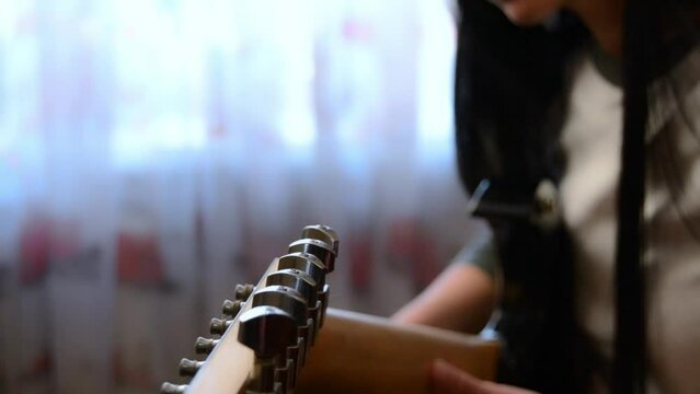 Closeup unrecognizable girl hands tuning guitar. Young woman checking pegs of guitar. Female guitarist tuning sound of musical instrument. Lady holding string instrument in hands