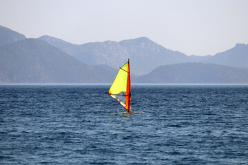 Windsurfing in the sea, water sports. View to windsurfer and green mountains in mist, scenic...