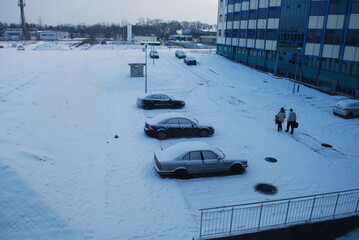 view of the building wall and parking and cars lot in winter, snow, sunlight breaking through the...