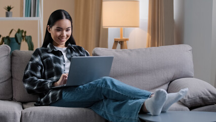Smiling asian woman using laptop casual browsing searching online play computer game. Korean...