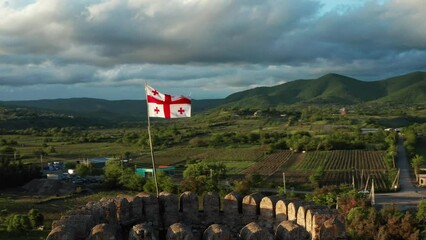 National flag of Georgia waving in wind on medieval fortress of Chailuri against backdrop of a valley, mountains. Kakheti Region, Georgia