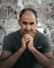 Portrait of senior 60-years old Turkish Cypriot man sitting leaning on hands on stone wall...