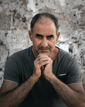 Portrait Of Senior 60-years Old Turkish Cypriot Man Sitting Leaning On Hands On Stone Wall Background