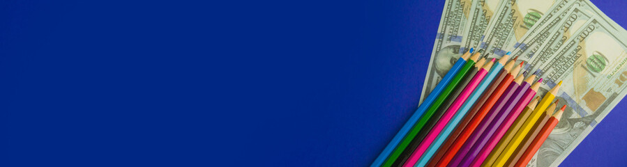 multicolored pencils on souvenir dollar bills. items lie on a blue background. Banner for insertion...