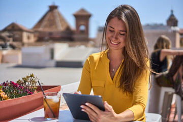 young happy woman working at her computer on the terrace of a Spanish café wearing a yellow blouse...