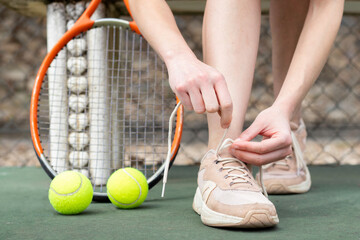 Close up detailed view of a person tying her shoelaces on on a tennis court with racket and balls...