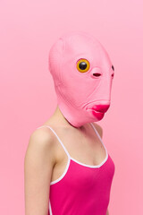 Funny crazy woman on a pink background standing in a fish head mask on a pink background, conceptual Halloween costume art photo