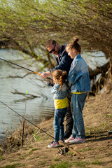A dad and his two daughters are fishing in the river. It's early spring outside. Family vacation. Hobby. Time with family. Together. Lifestile.