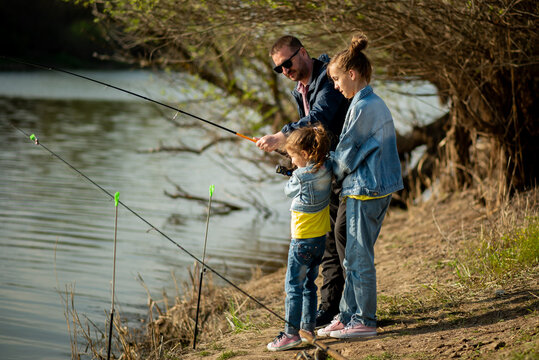 A dad and his two daughters are fishing in the river. It's early spring outside. Family vacation. Hobby. Time with family. Together. Lifestile.