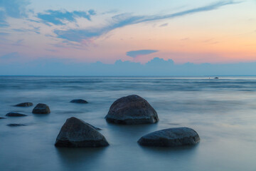 Fototapeta na wymiar Rocky shore with stones sinking in the sea water. Sunset, long exposure. Baltic sea