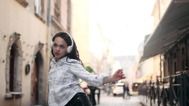 Young beautiful woman with dreadlocks listening music and dancing in the city centre. Slow motion of happy young woman in headphones dancing outdoors in city street.