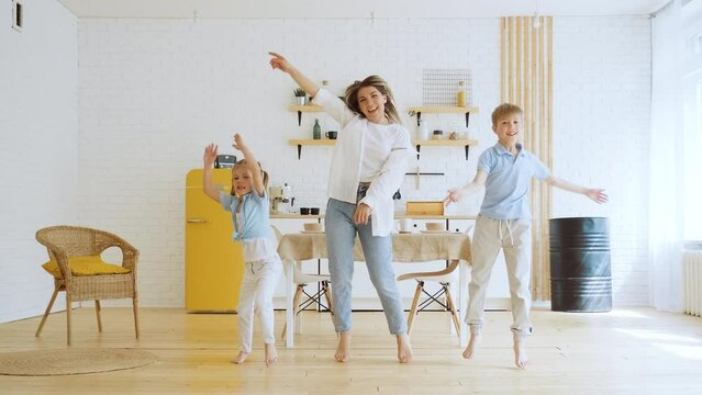 Happy emotional dance of mother with her two children, active modern family enjoy activities at home in living room. Motherhood and childhood, listening to music together, having fun