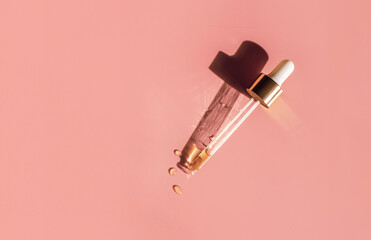 Pipette with gold metallic cap and drops of water, serum, oil, beauty product on warm pink background. Natural medicine, cosmetic research, bio science. Concept of skincare and analysis. Flat lay