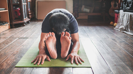 Young Asian man practicing yoga, sitting in Seated forward bend exercise, paschimottanasana pose on...