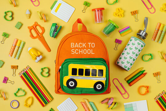 Kids Backpack with school bus on yellow background. Opened School backpack with stationery. Primary School or kindergarten.