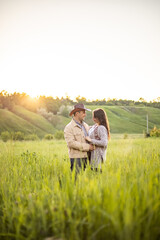 Fototapeta na wymiar young beautiful couple, standing on a green meadow in the rays of the setting sun, cowboy clothes.rustic style