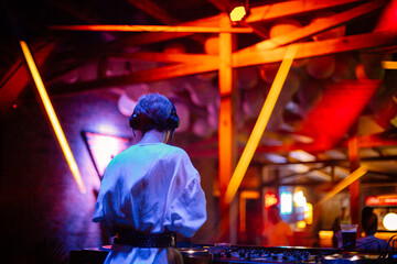 girl dj plays a set in a nightclub. girl dj at the dj console against the backdrop of a nightclub,...