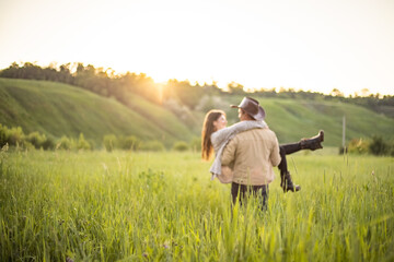 Fototapeta na wymiar young beautiful couple, on a green meadow in the rays of the setting sun, a man holds a girl in his arms, cowboy clothes.rustic style
