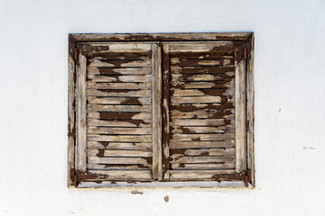 Old wooden window with shutters on an old cracked white wall.
