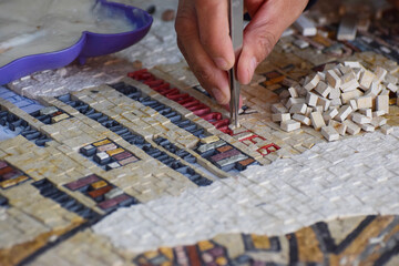 A close up of the hand of a Jordanian mosaic artist making an intricate mosaic using small tiles...