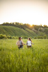 Fototapeta na wymiar young beautiful couple, on a green meadow in the rays of the setting sun, a man and a girl run towards the camera, cowboy clothes. rustic style